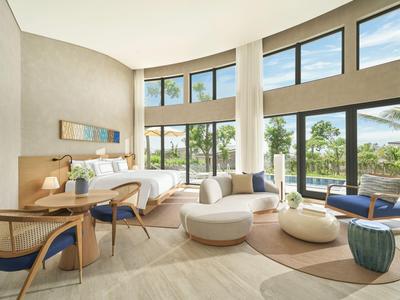 Chambre d'hôtel moderne avec grandes fenêtres, mobilier clair et vue sur un paysage verdoyant.