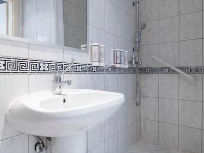 Helles Bad mit weißem Waschbecken und separater Duschkabine mit Glasabtrennung.