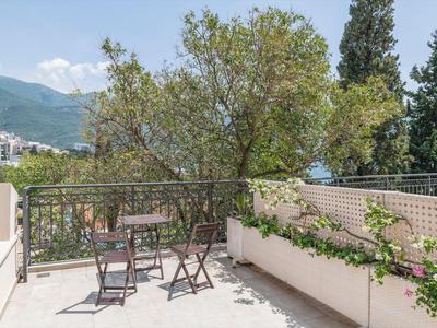 Balkon mit kleinem Holztisch und Stühlen, umgeben von Pflanzen und Blick auf Berge.