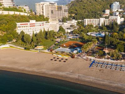 Strand mit Sonnenliegen und Hotels im Hintergrund an einem bewaldeten Hügel