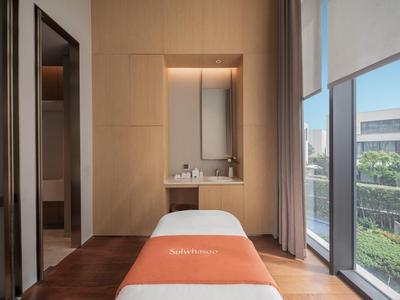 Sala de masajes luminosa con camilla y grandes ventanas con vista a jardines.