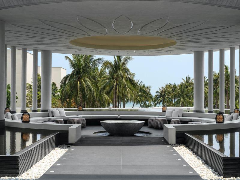 Lounge moderna de hotel con fuentes, áreas de sofá y vistas a palmeras al fondo