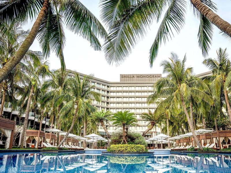 Hotel con palmeras altas y una gran piscina en primer plano bajo luz diurna brillante