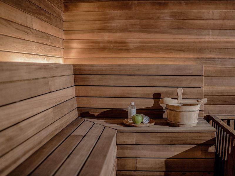 Sauna de madera con bancos, cubo, cucharón y botella aromática sobre la mesa.