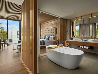 Habitación de hotel moderna con bañera independiente, cama doble y grandes ventanales con vista a la ciudad.