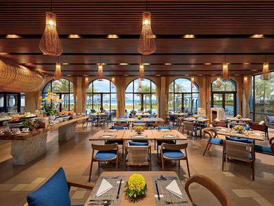 Modern eingerichtetes Wohnzimmer mit Sofa, Sessel, Esstisch und großen Fenstern.