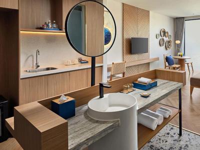 Habitación de hotel moderna con área de lavado abierta, muebles de madera y zona de estar.