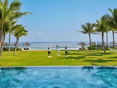 Grünes Resort mit Pool, Palmen und drei Personen, die den Ozean im Hintergrund genießen.