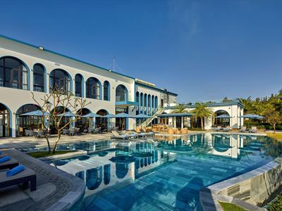 Piscina moderna del hotel con tumbonas y agua azul clara bajo un cielo soleado.