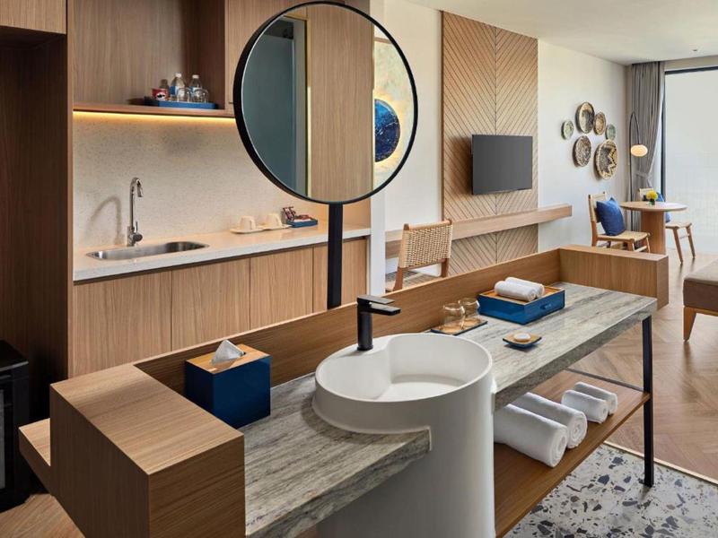 Habitación de hotel moderna con área de lavado abierta, muebles de madera y zona de estar.