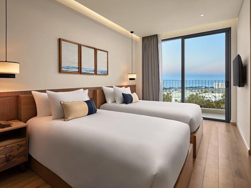 Habitación de hotel moderna con dos camas, muebles de madera y vista al mar a través de grandes ventanas.