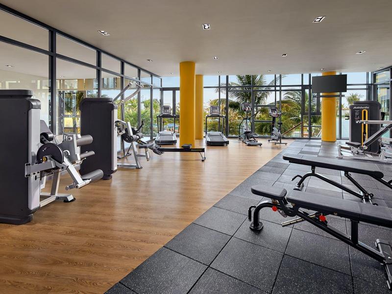 Gimnasio grande con ventanales, equipos modernos y suelos de madera y goma.