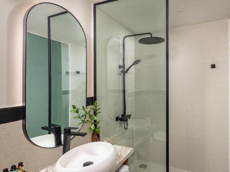 Baño moderno de hotel con espejos redondos, ducha de vidrio y lavabo de mármol.