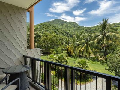 Balcón con sillas y mesa con vistas a vegetación tropical y montañas al fondo.