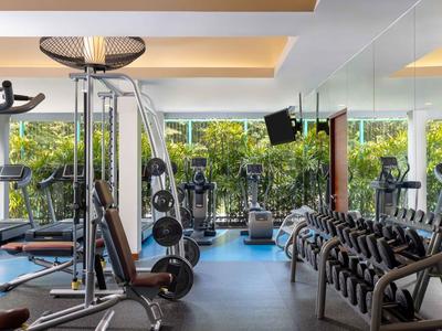 Moderner Fitnessraum mit verschiedenen Trainingsgeräten und Hanteln vor großen Fenstern.