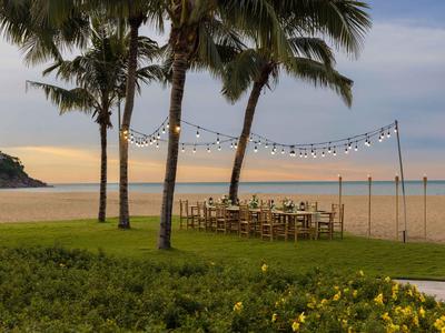 Strandrestaurant mit Holztischen und Stühlen unter Palmen bei Sonnenuntergang.