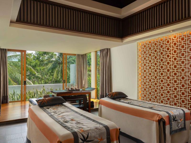 Habitación moderna con dos camillas de masaje y vista a un balcón con árboles.