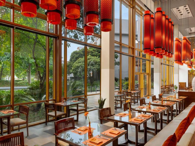 Restaurante moderno con grandes ventanales y lámparas rojas, con vista a árboles verdes.