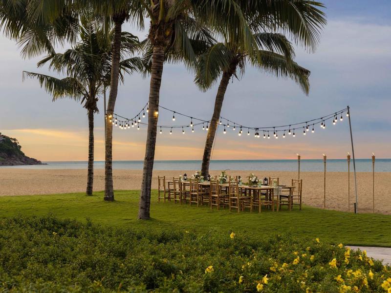 Playa con palmeras y mesa puesta bajo luces colgantes al atardecer