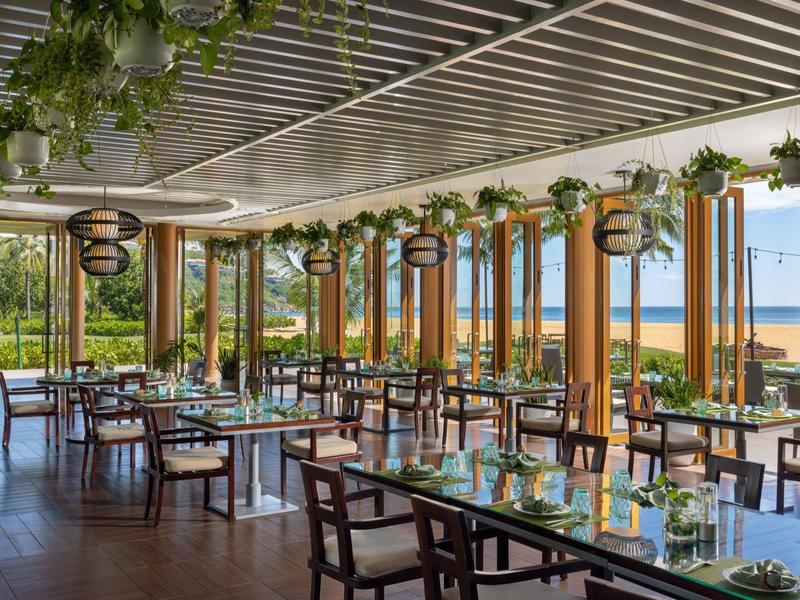 Restaurante luminoso con grandes ventanas, sillas de madera y vista al mar en el fondo.