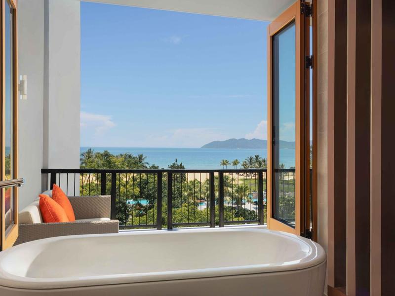 Bañera independiente en balcón con vista al mar y montañas bajo cielo despejado.