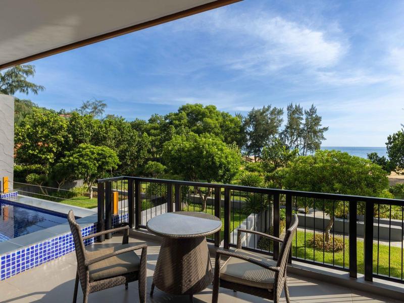 Balcón con mesa y dos sillas con vista a árboles verdes y cielo azul