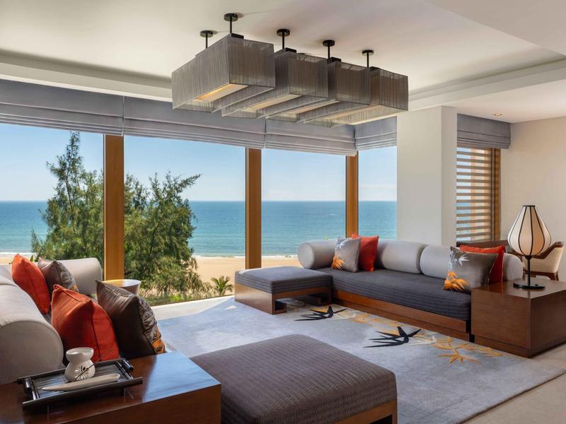 Sala moderna con grandes ventanas y vista al mar decorada con muebles grises y naranjas.