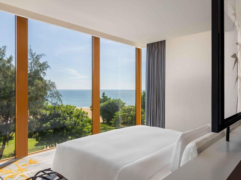 Habitación de hotel moderna con vistas al jardín y al mar a través de grandes ventanas.