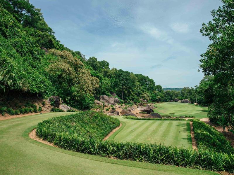 Campo de golf verde bien cuidado rodeado de árboles bajo un cielo nublado.