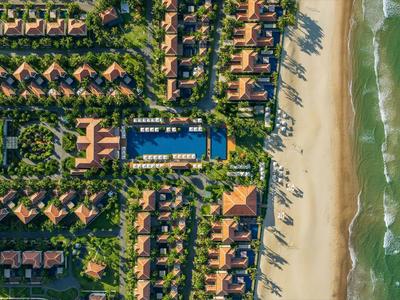 Luftaufnahme eines Strandresorts mit Reihen von Bungalows, Pool und grünem Garten neben dem Meer.