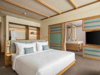 Camera d'hotel moderna con letto grande, TV, scrivania e rivestimenti in legno minimalisti.