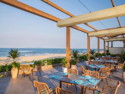 Offener Essbereich mit Holzstühlen und Blick auf das Meer unter einem Pergolendach.
