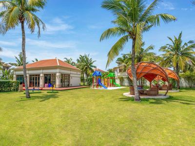 Giardino dell'hotel con prato, palme, gazebo e area giochi colorata sotto il sole.