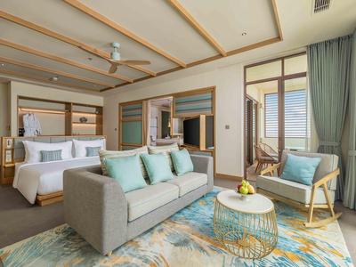 Camera d'hotel luminosa con letto matrimoniale, divano, poltrona e balcone con vista mare.