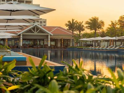Poolbereich eines Resorts mit Liegestühlen und Sonnenschirmen bei Sonnenuntergang