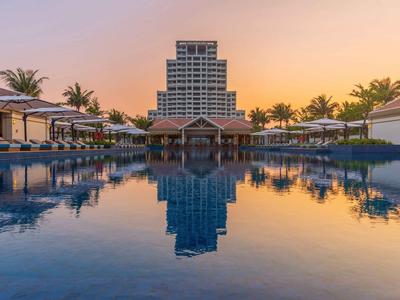 Moderner Hotelkomplex mit großem Pool und Palmen bei Sonnenuntergang.