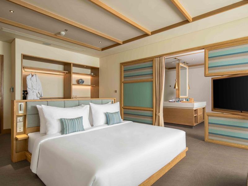 Camera d'hotel moderna con letto grande, TV, scrivania e rivestimenti in legno minimalisti.