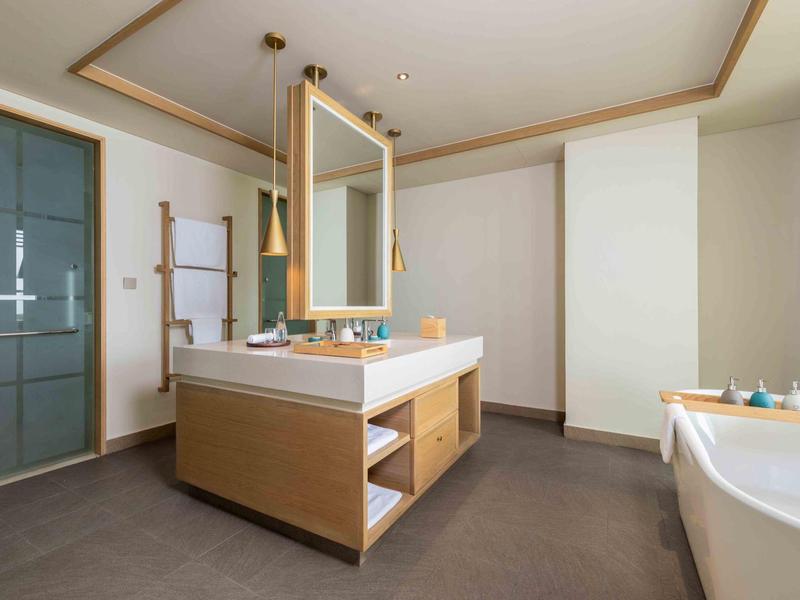 Bagno moderno con grande vasca, lavabo e armadi in legno dal design neutro.