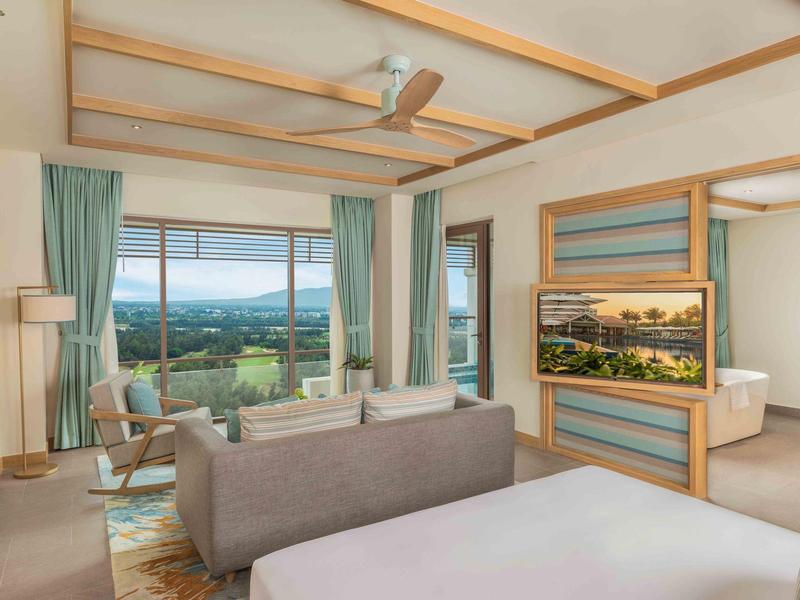 Camera d'hotel moderna con finestre panoramiche, vista sul paesaggio, area salotto e bagno aperto.