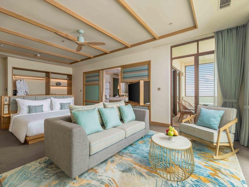 Camera d'hotel luminosa con letto matrimoniale, divano, poltrona e balcone con vista mare.