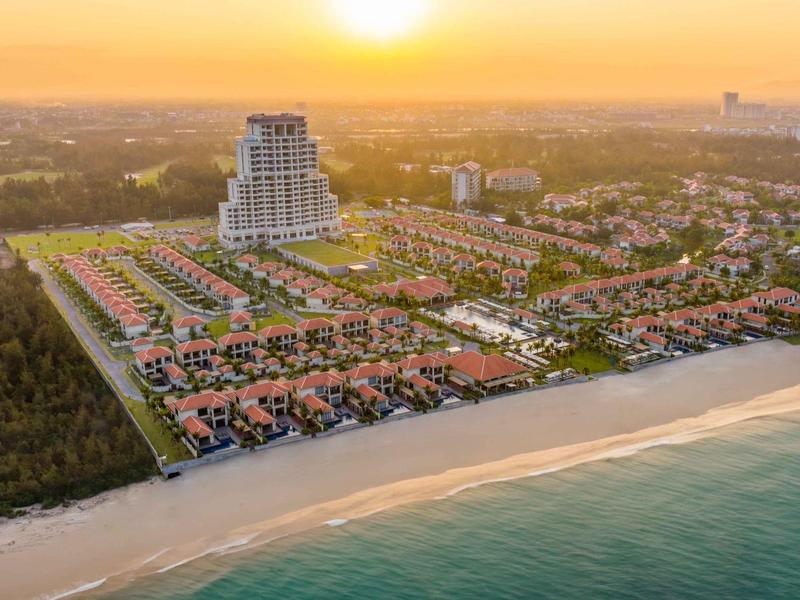 Vista aerea di un hotel e ville sulla spiaggia al tramonto.