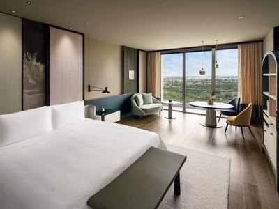 Modern eingerichtetes Hotelzimmer mit großem Bett, Sitzbereich und Panoramafenster mit Aussicht.
