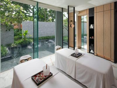 Modernes Spa mit zwei Massageliegen vor bodentiefen Fenstern und Blick auf Garten.