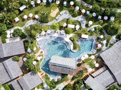 Vogelperspektive eines unregelmäßig geformten Pools mit Sonnenschirmen und umliegenden Gebäuden.