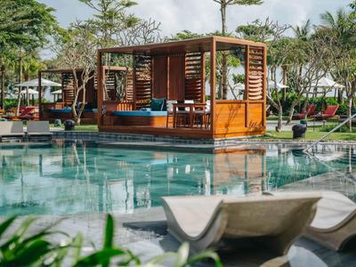 Ein Swimmingpool mit Holzpavillon und Liegestühlen in einer tropischen Hotelanlage.