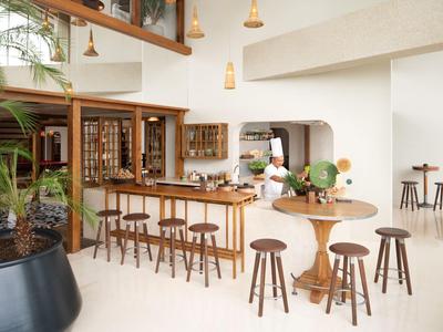 Helles Hotelrestaurant mit Holztheke, Barhockern und rundem Tisch mit Stühlen.