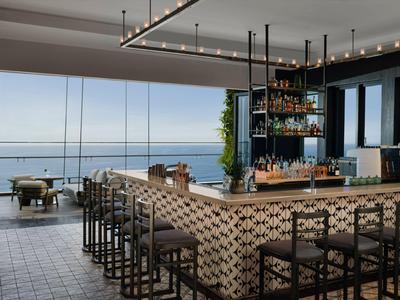 Moderner Hotelbarbereich mit gemustertem Tresen und Blick auf das Meer durch Glasfront.
