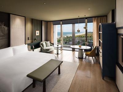 Modernes Hotelzimmer mit großem Bett, Sitzbereich und Panoramafenstern mit Stadtblick.