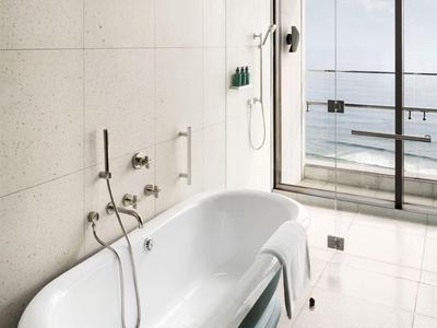 Moderne Badewanne vor Glaswand mit Balkon und Meerblick in einem Hotelzimmer.