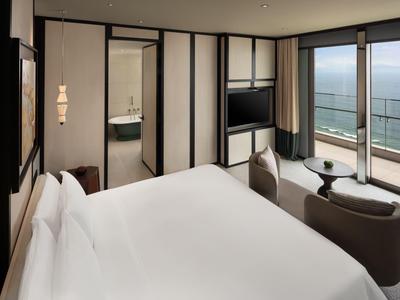 Modernes Hotelzimmer mit Doppelbett, Sitzecke und großem Fenster mit Meerblick.